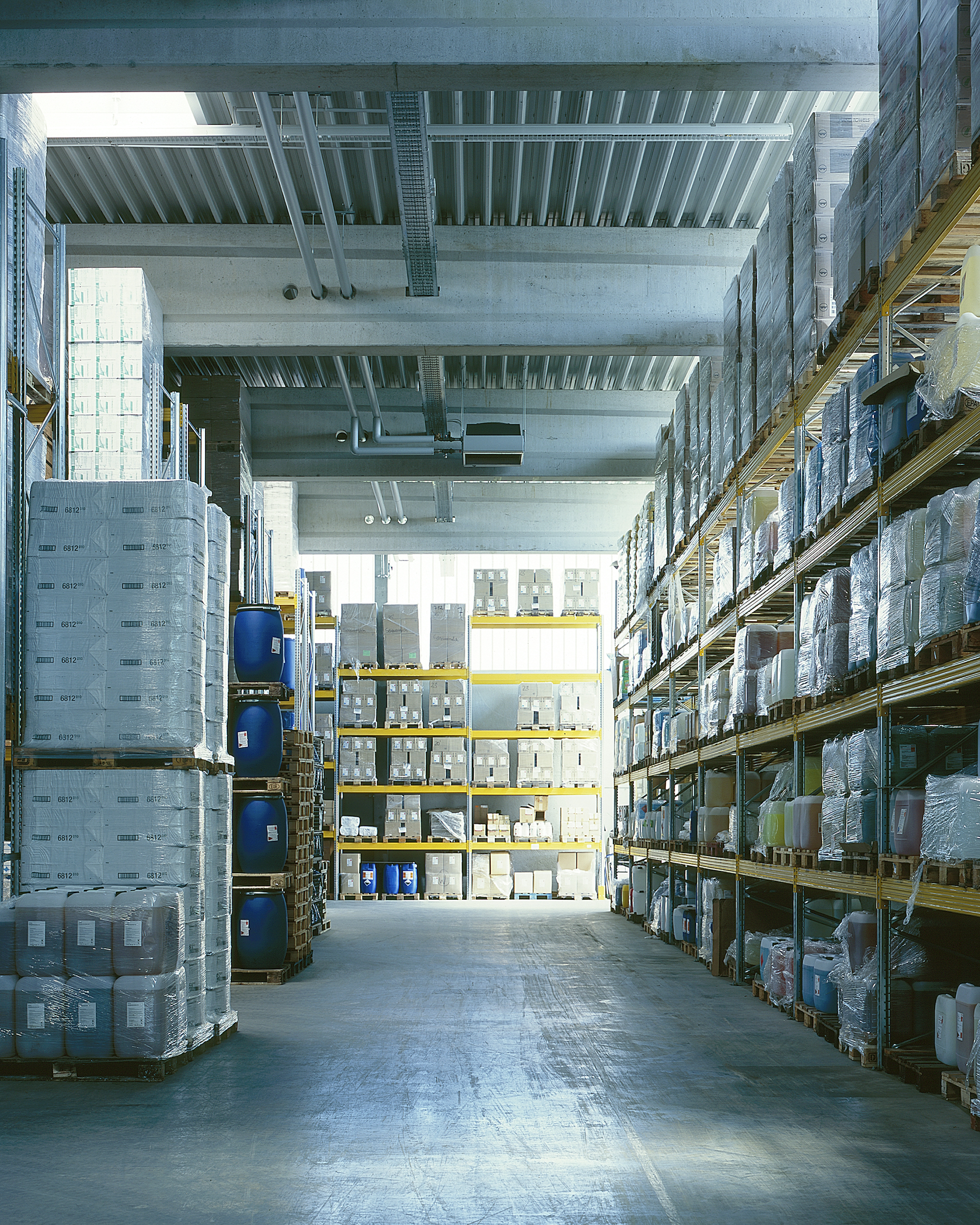 Logistik- und Anlieferungsbereich mit Laderampen, Büroanbau und geparkten Fahrzeugen vor der Halle von „Layer-Chemie“.