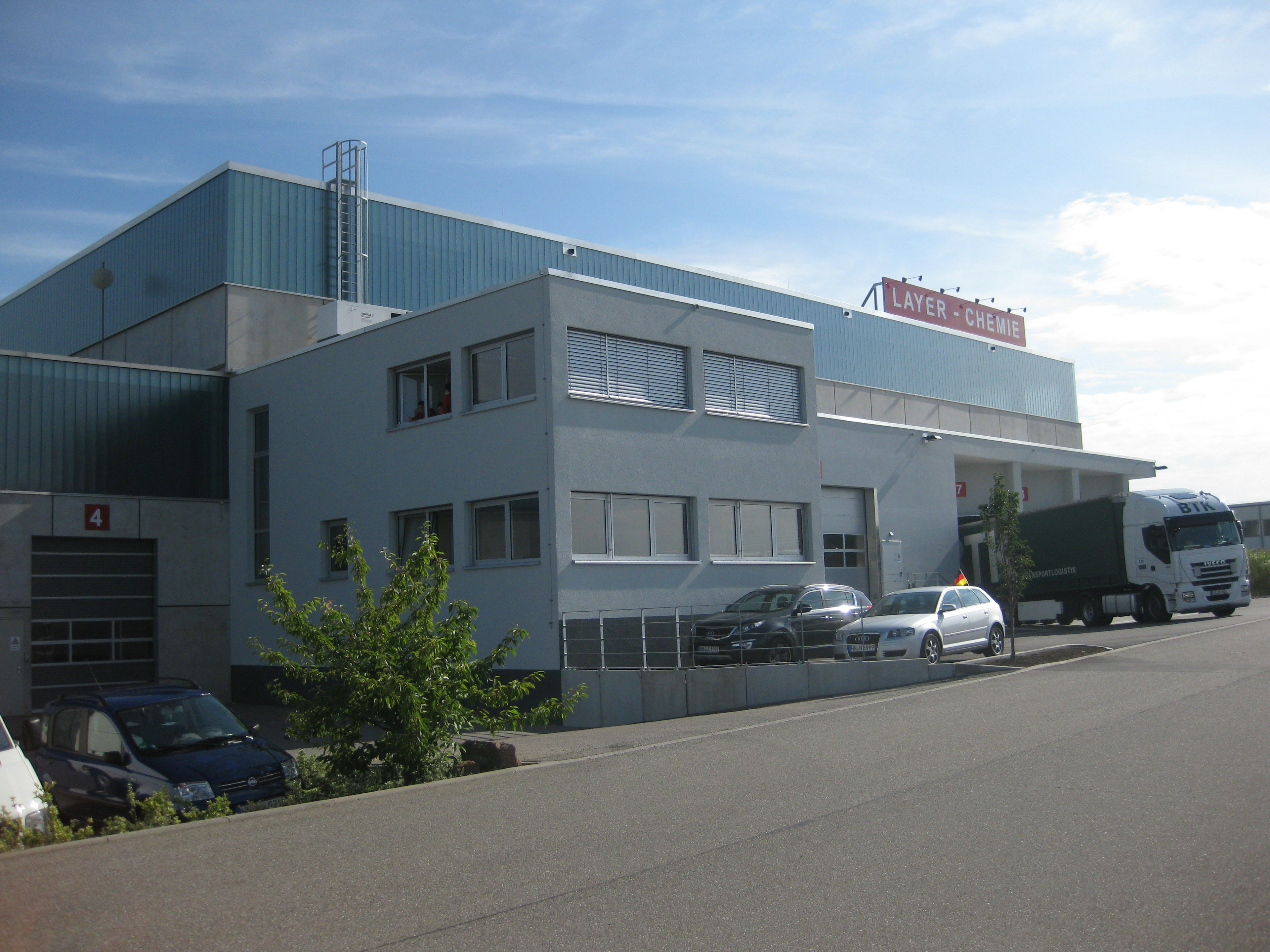 Rückseite des Gebäudes mit klar strukturierter Fassade, kleinen Bürofenstern und angrenzender Wildblumenwiese.