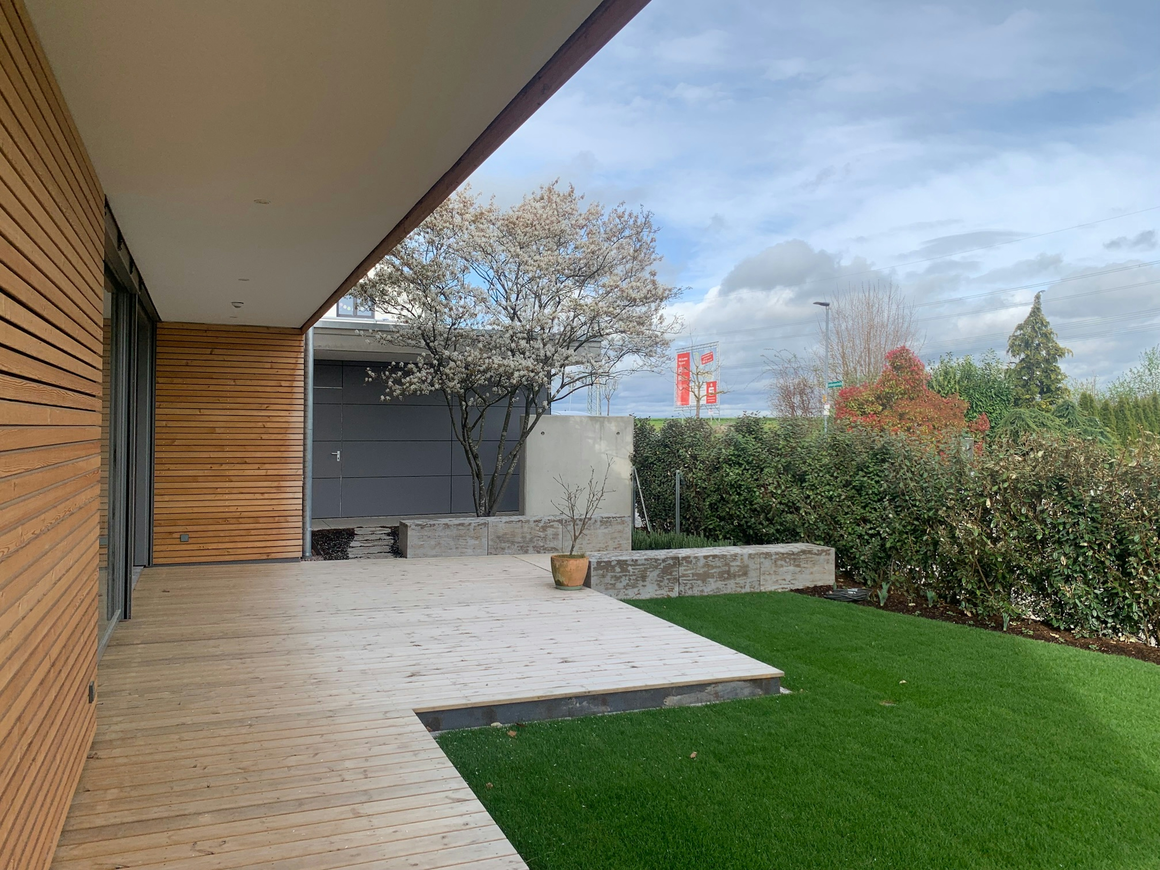 Großzügige Holzterrasse mit Blütenbaum und Sichtschutzhecke – moderner Außenbereich des Neubaus mit Blick in den Garten.