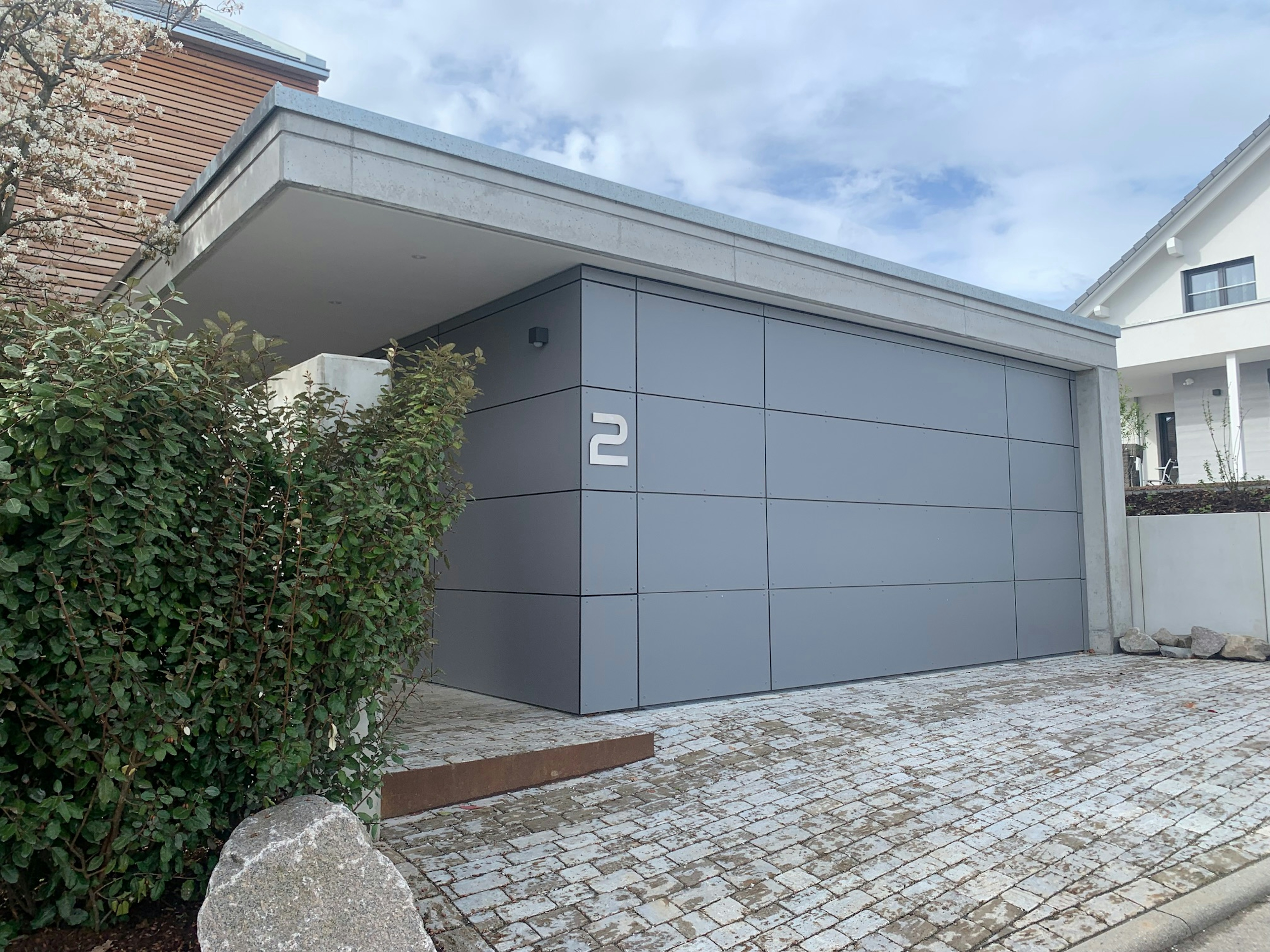 Seitliche Ansicht des Eingangsbereichs mit grauer Garage und Hausnummer 2 – klar strukturierte, moderne Fassadengestaltung.
