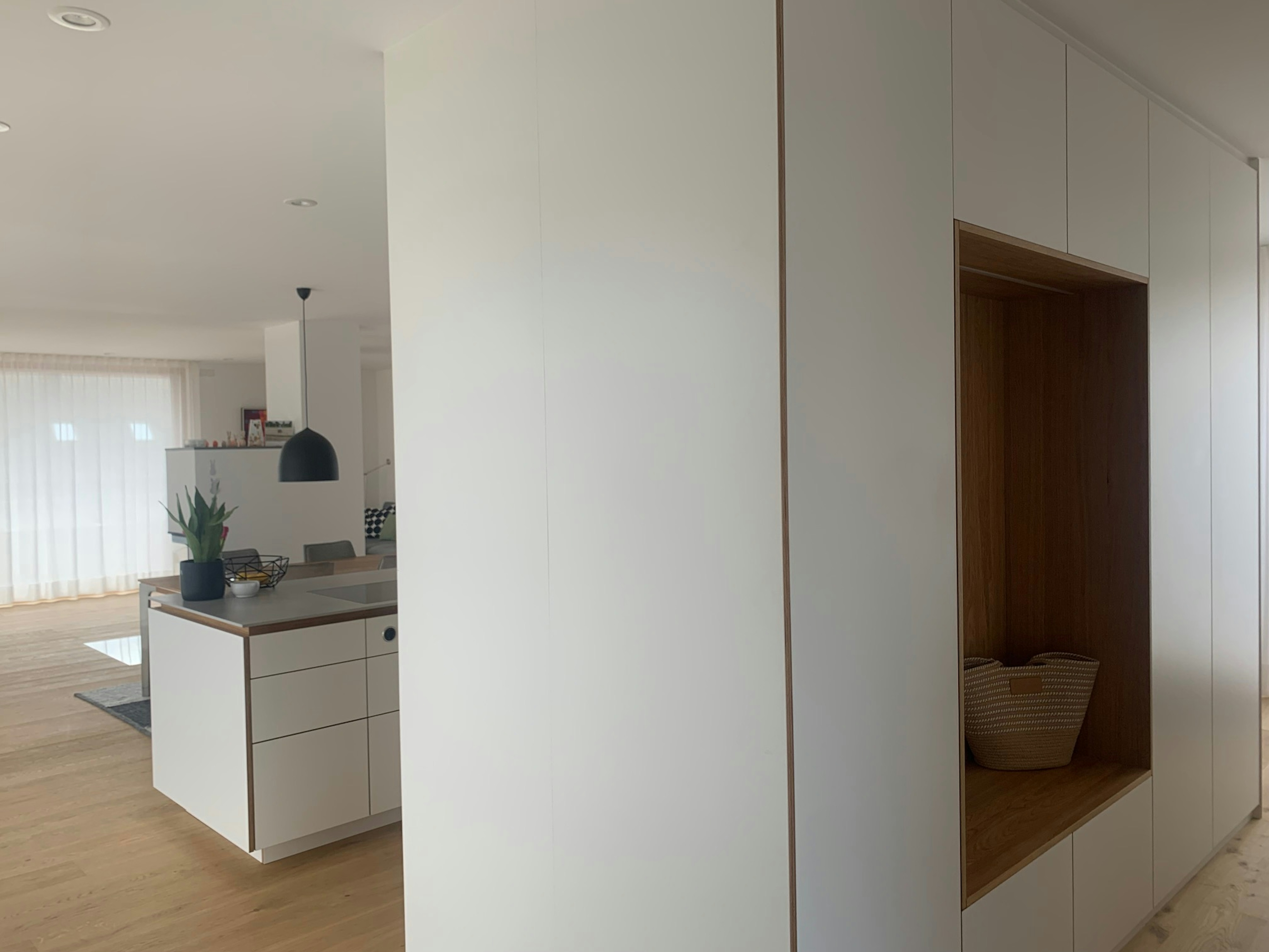 Helle, offene Küche mit weißen Fronten, Holzdetails und klarer Linienführung – modernes Wohnkonzept mit viel Stauraum