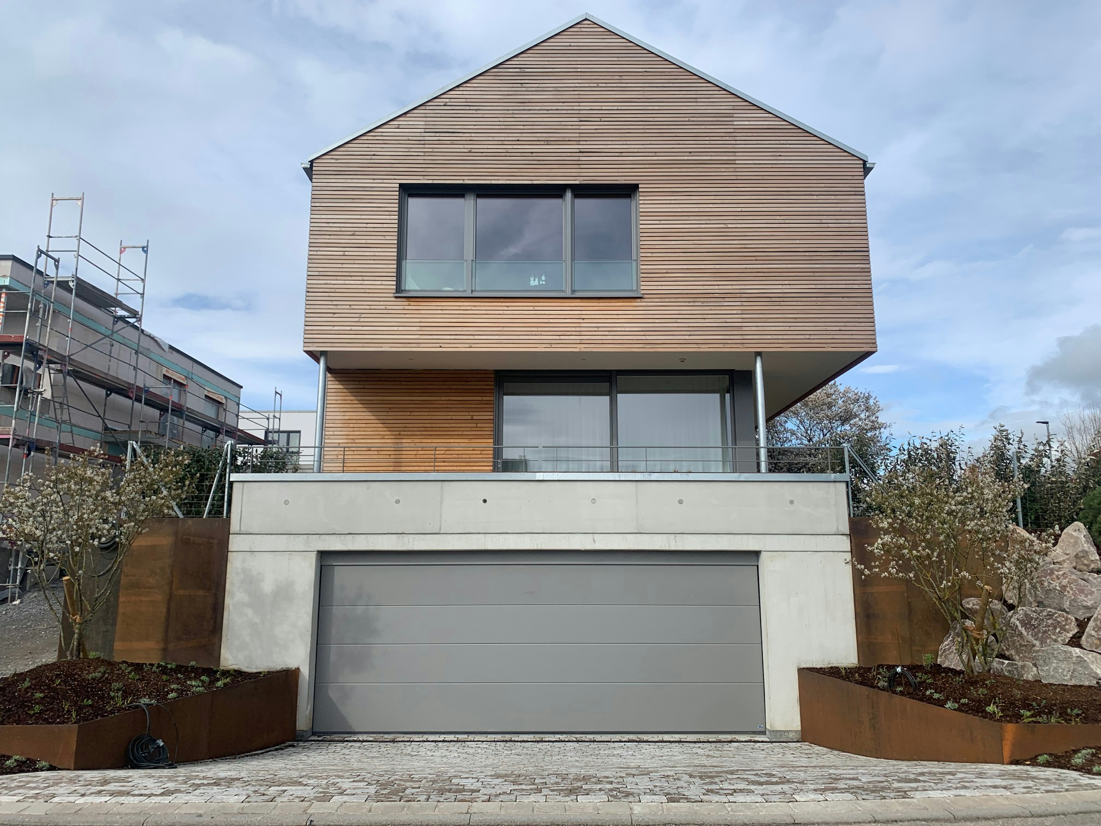 Vorderansicht des Einfamilienhauses mit Satteldach und Holzverkleidung, kombiniert mit Sichtbeton und großen Fensterflächen.