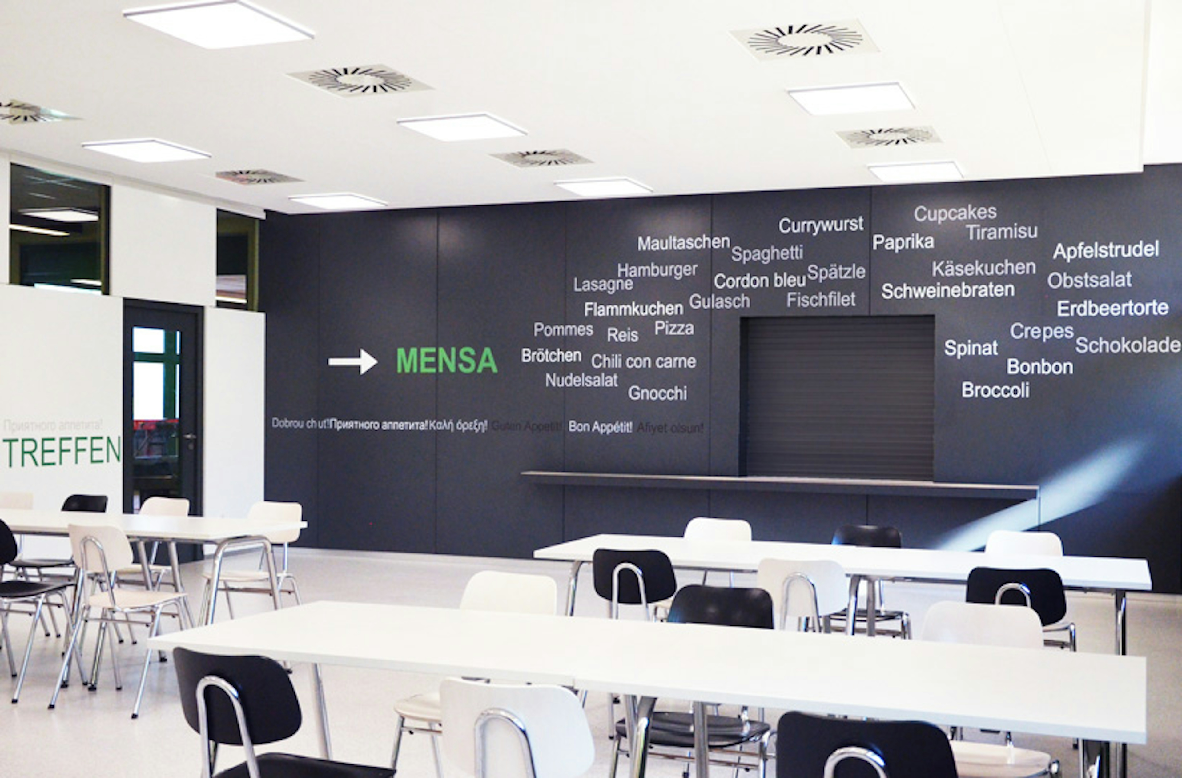 Modernisierte Mensa mit grafisch gestaltetem Leitsystem, Deckenbeleuchtung und schlichtem Möbeldesign – Umbau durch Architekturbüro Bauer.
