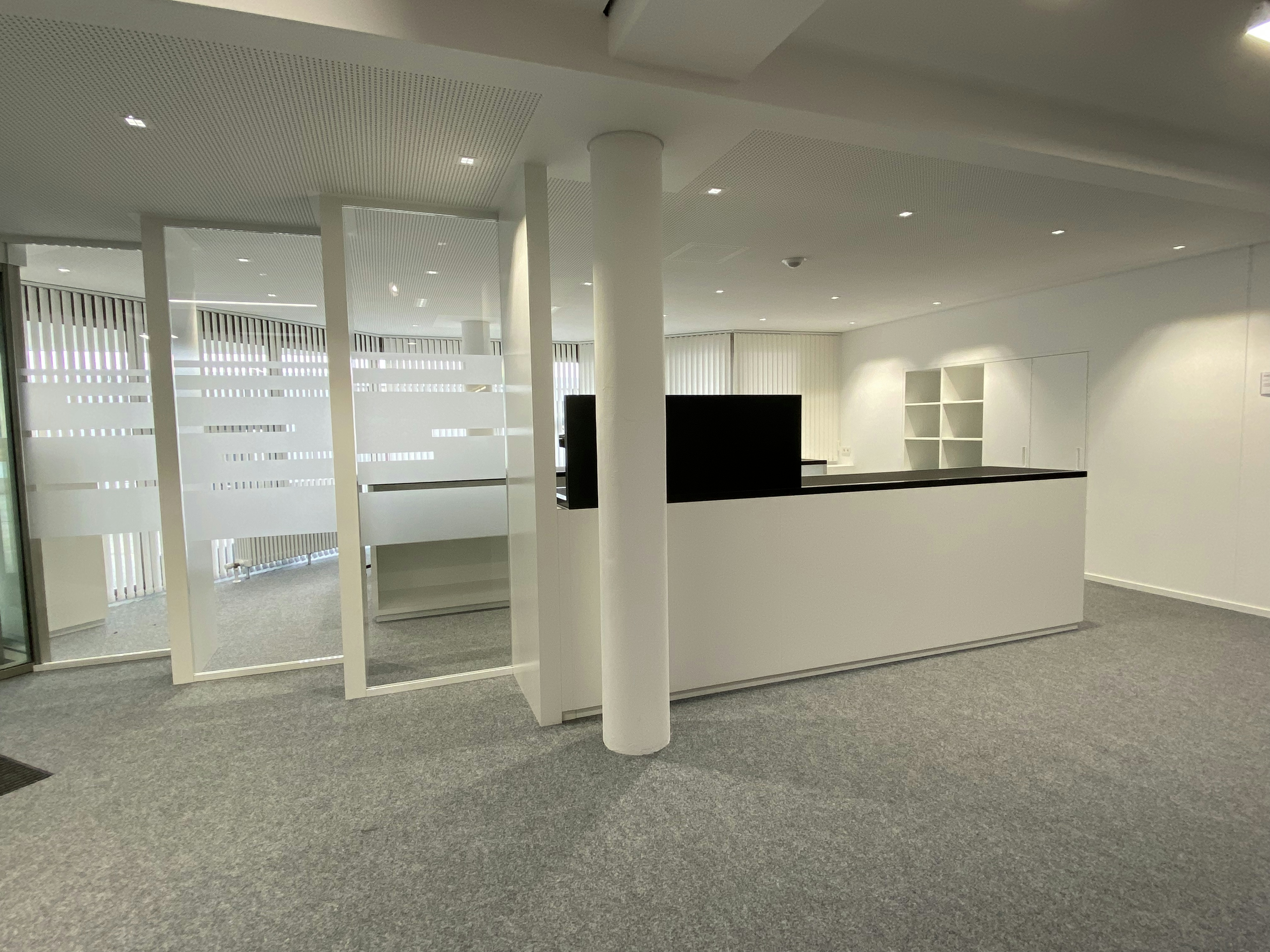 Empfangstresen mit dunkler Arbeitsplatte und offenen Regalfächern, umgeben von modernen Büroflächen im Kreismedienzentrum Heilbronn.