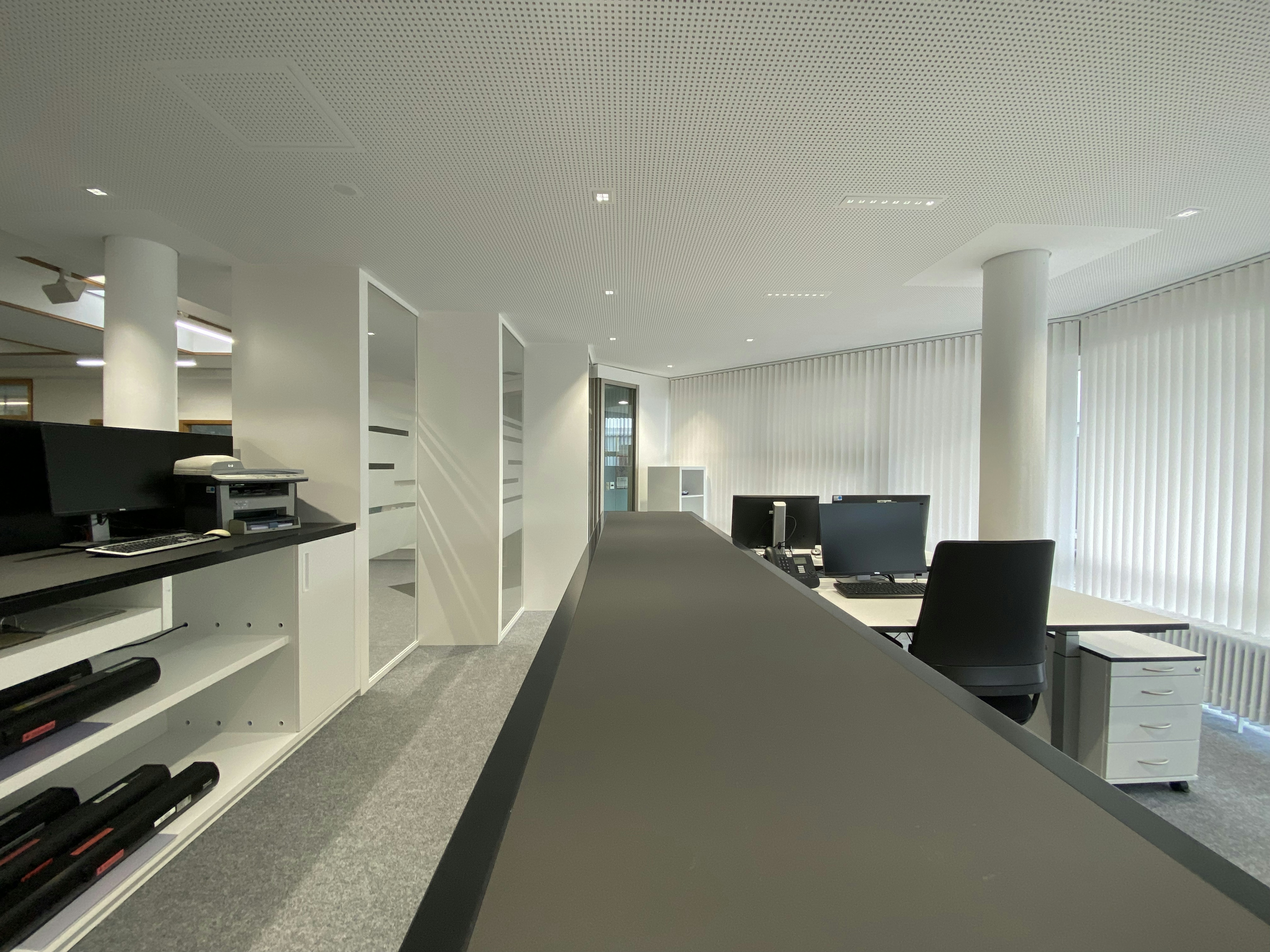 Klar strukturierter Flurbereich mit Glaswänden und integrierten Sichtschutzstreifen, angrenzend an moderne Büroarbeitsplätze.