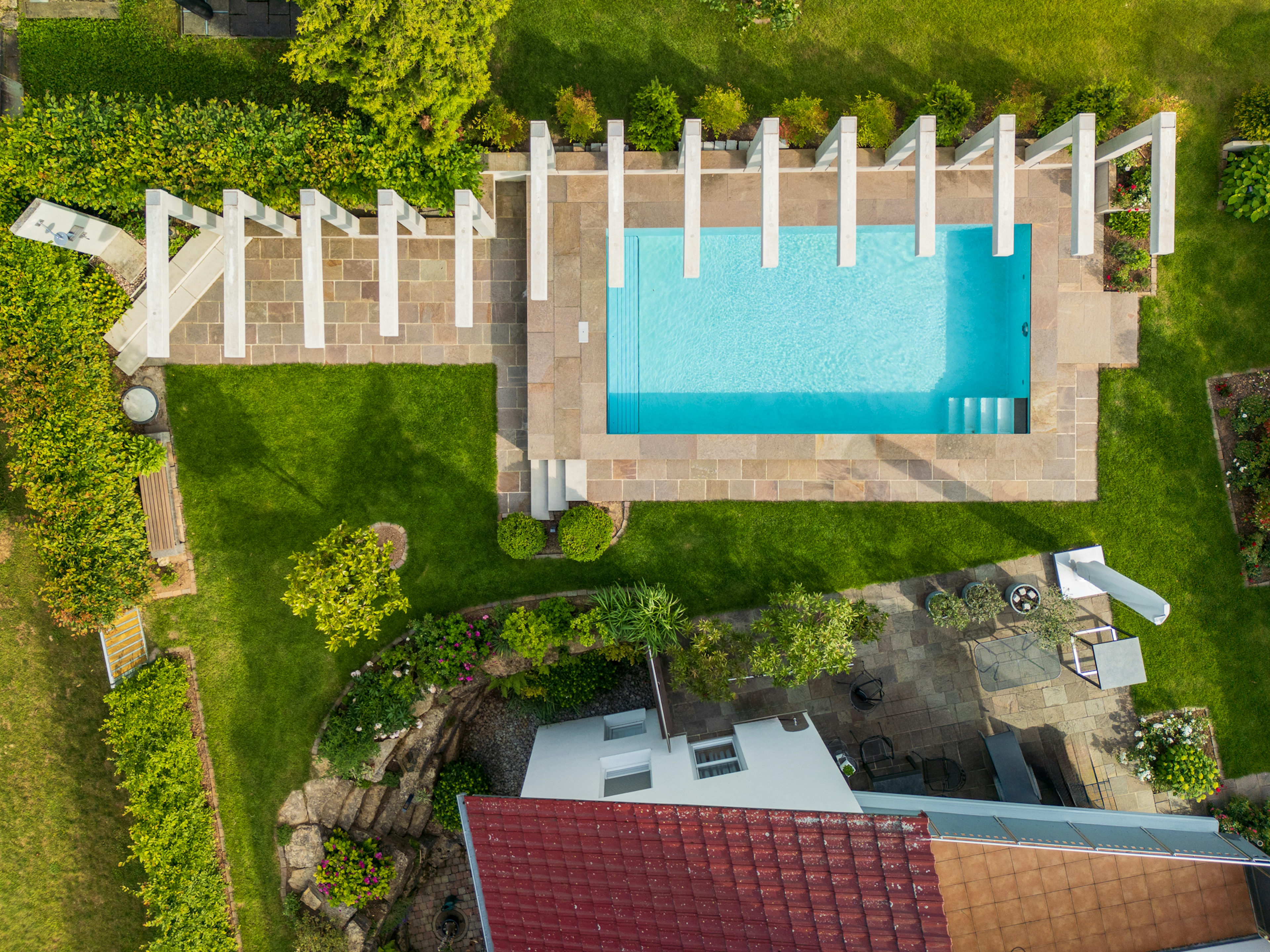 Luftaufnahme der gesamten Außenanlage mit Pool, Gartenwegen, Terrassenmöbeln und symmetrischer Pergolakonstruktion