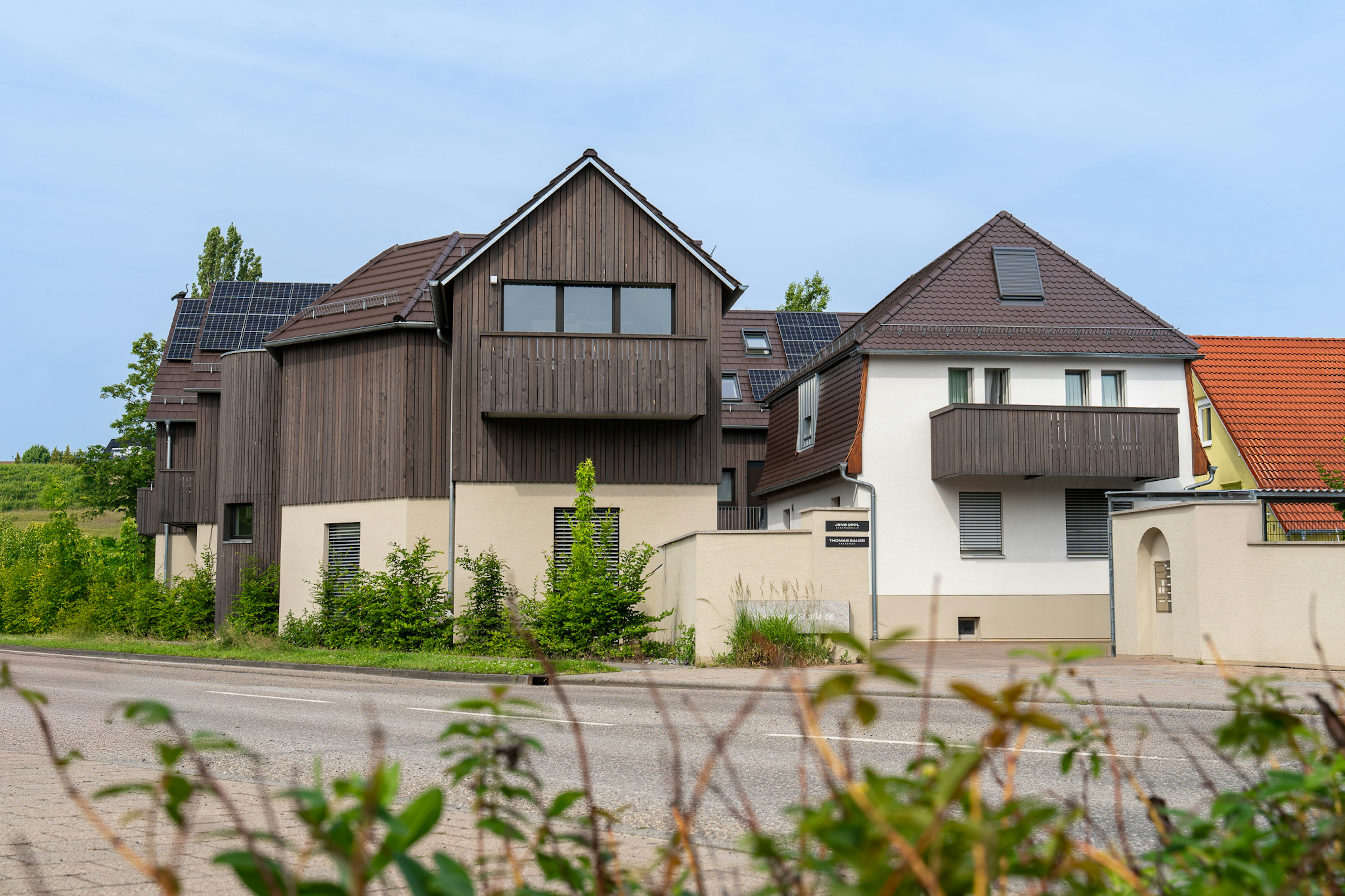 Frontansicht des Projekts mit Blick auf den Übergang vom Altbestand (Putzfassade) zum Neubau (Holzfassade) und Beschilderung zum Architekturbüro.