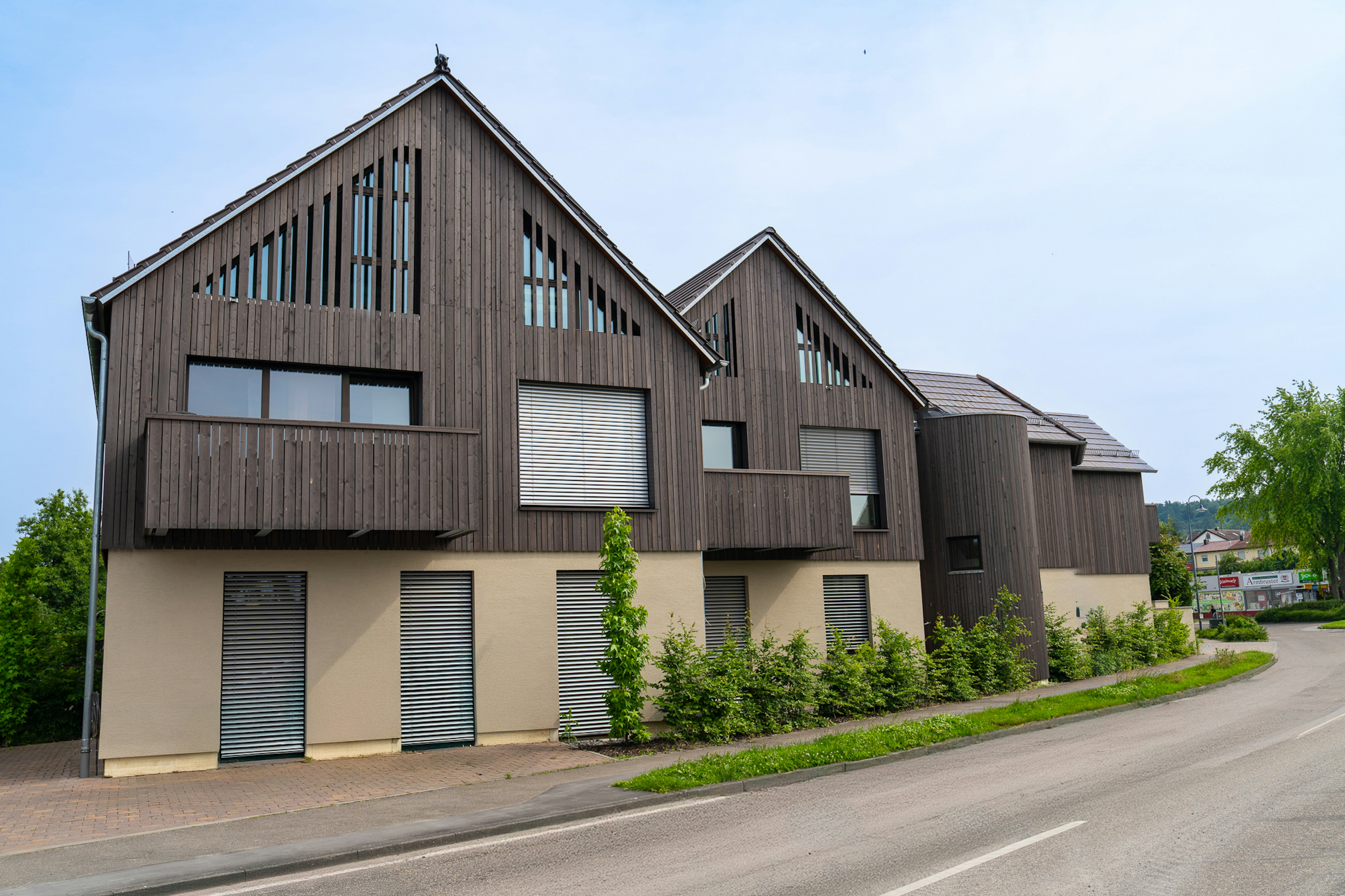 Straßenansicht der modernisierten Wohngebäude mit dunkler Holzfassade, Balkonen und großen Fensteröffnungen.