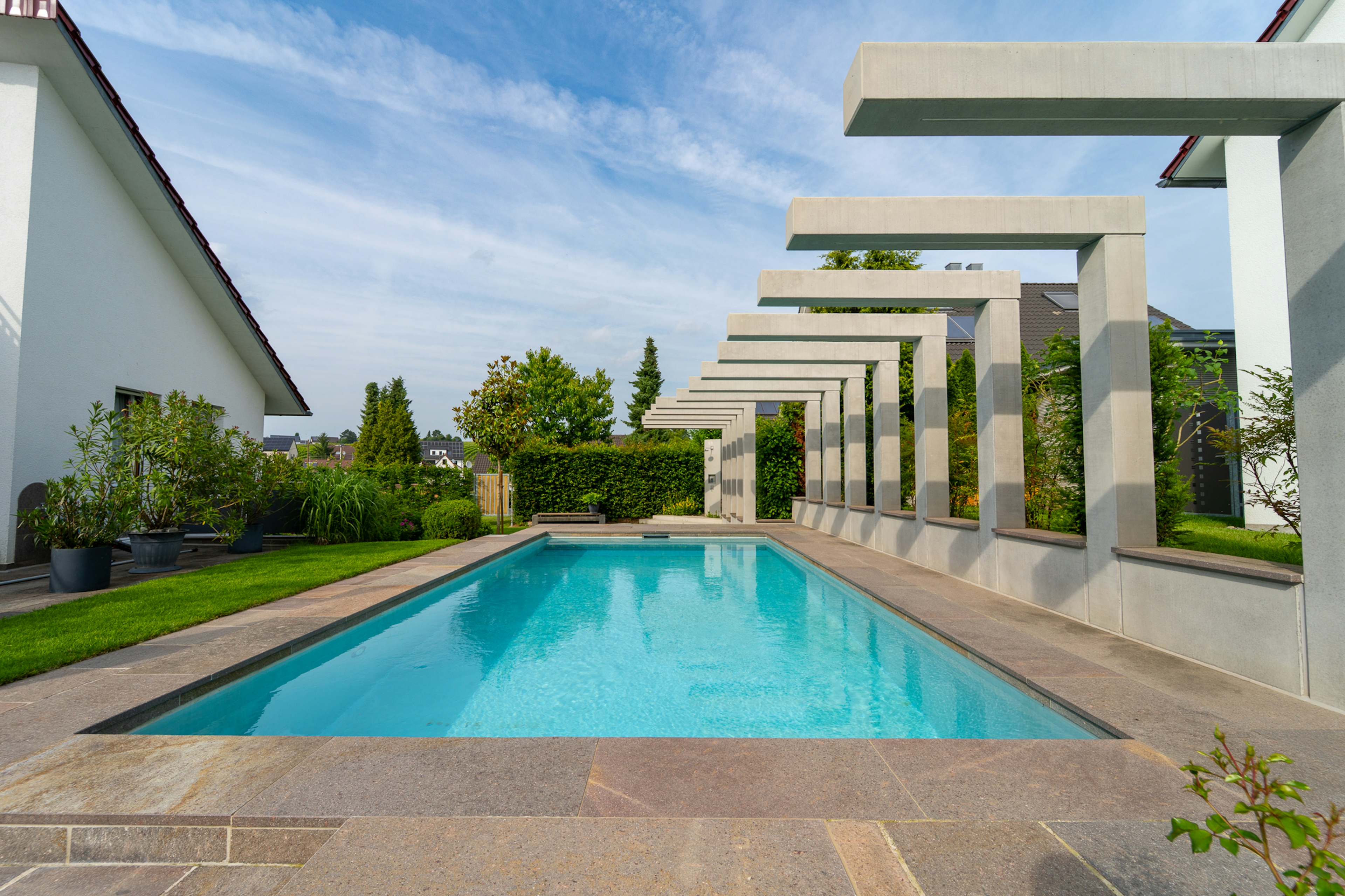 Symmetrischer Blick entlang der Pergola-Struktur mit reflektierendem Wasser im Mittelpunkt, Gartenpflanzen im Hintergrund