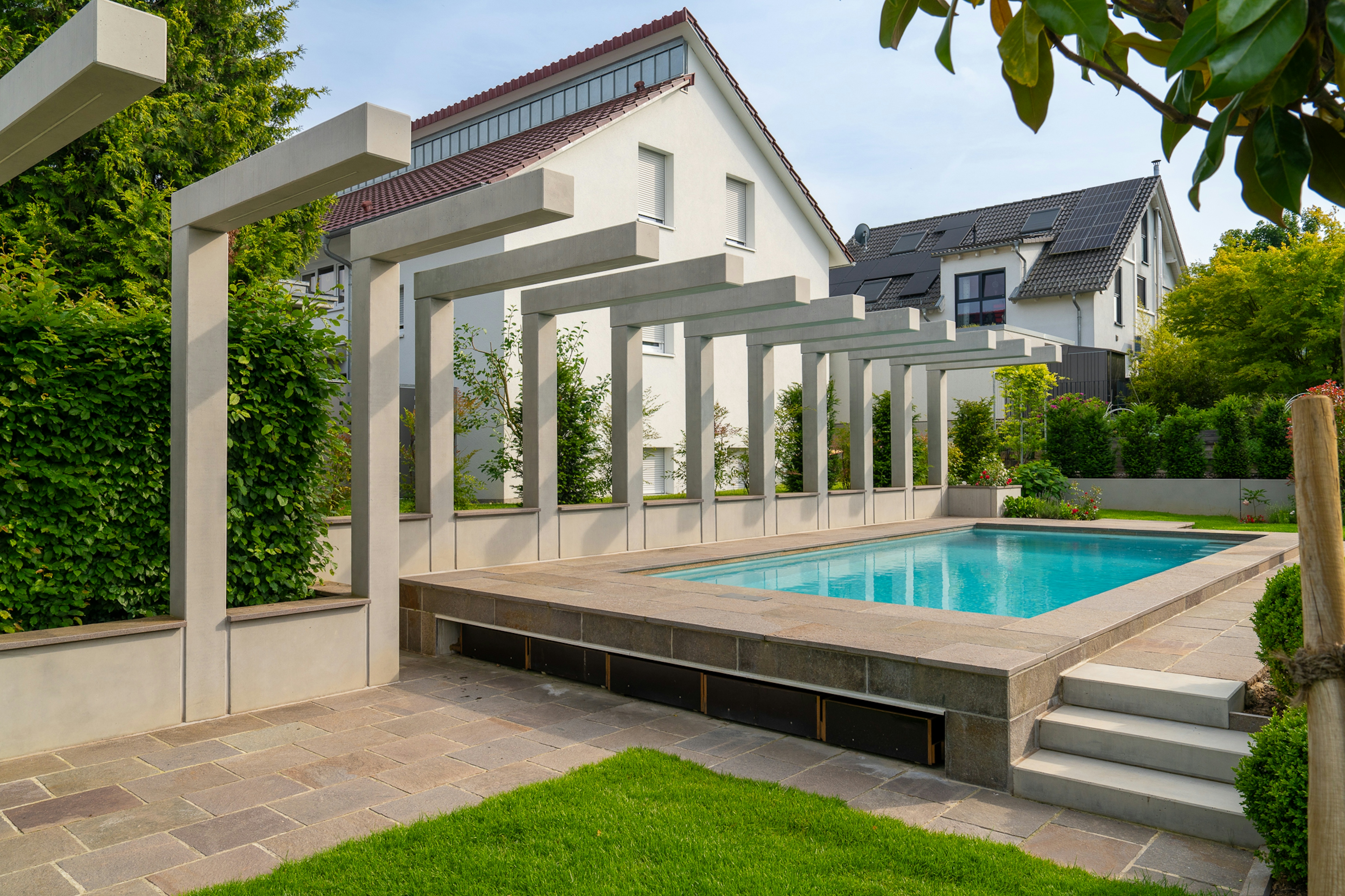 Moderner Garten mit Poolanlage, Sichtbeton-Pergola und gepflegtem Rasen in Wohnsiedlung