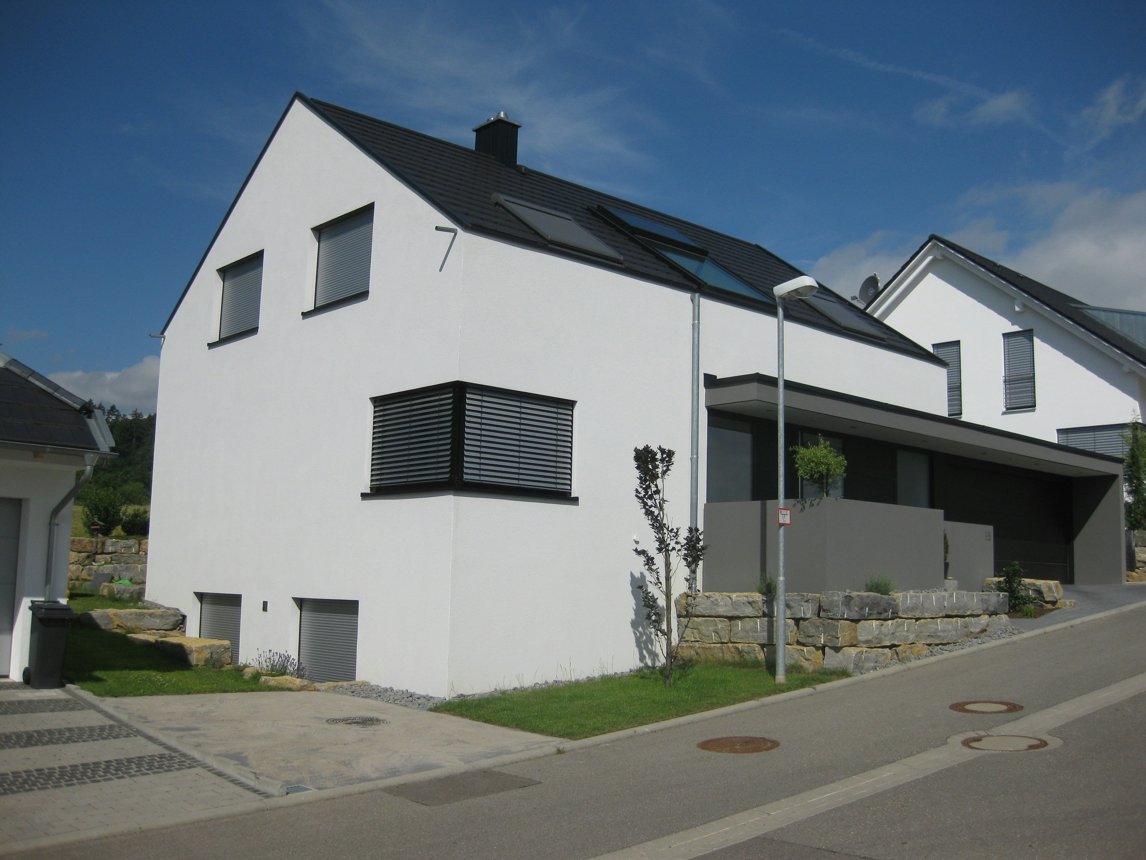 Rückseitige Gartenansicht eines minimalistischen Wohnhauses mit großen Glasflächen und Sichtschutz durch Begrünung.