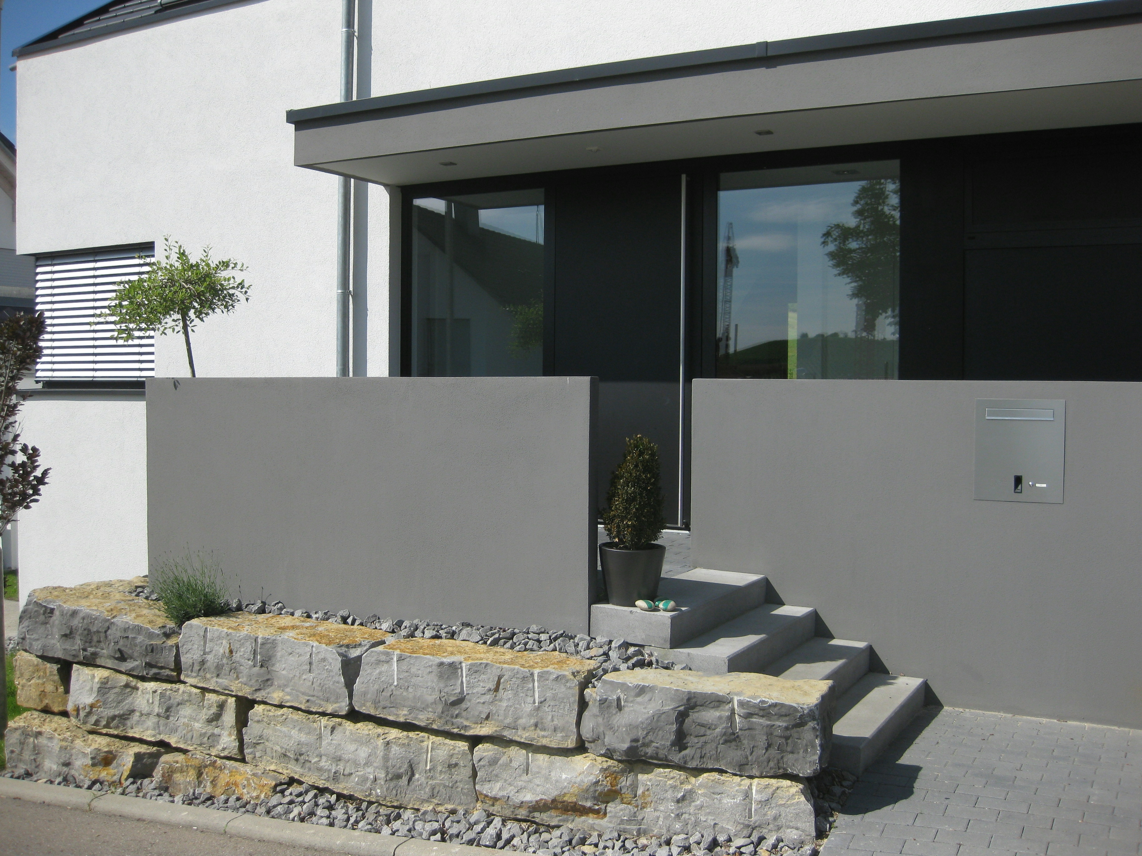 Blick auf den Eingangsbereich mit Sichtbetonelementen und harmonischer Verbindung von Architektur und Außenraumgestaltung.