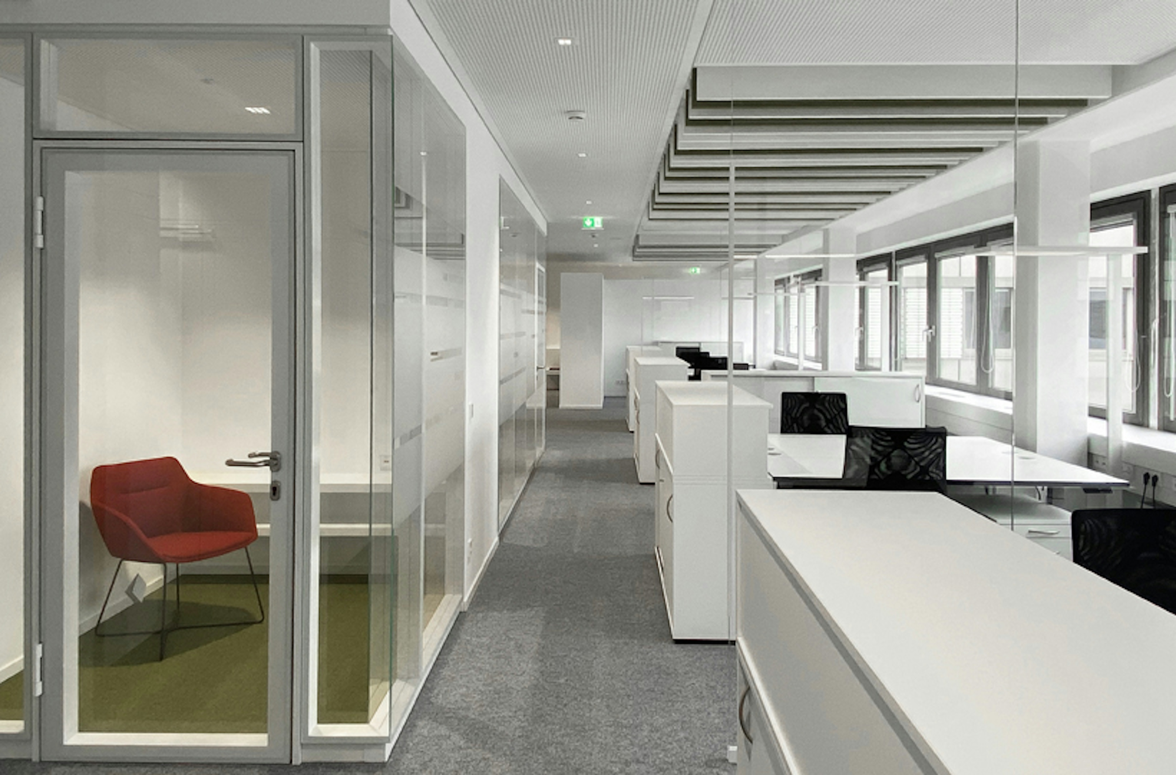 Offenes Büro mit klarer Struktur, Glaswänden und einem abgetrennten Raum mit einem roten Lounge-Sessel.