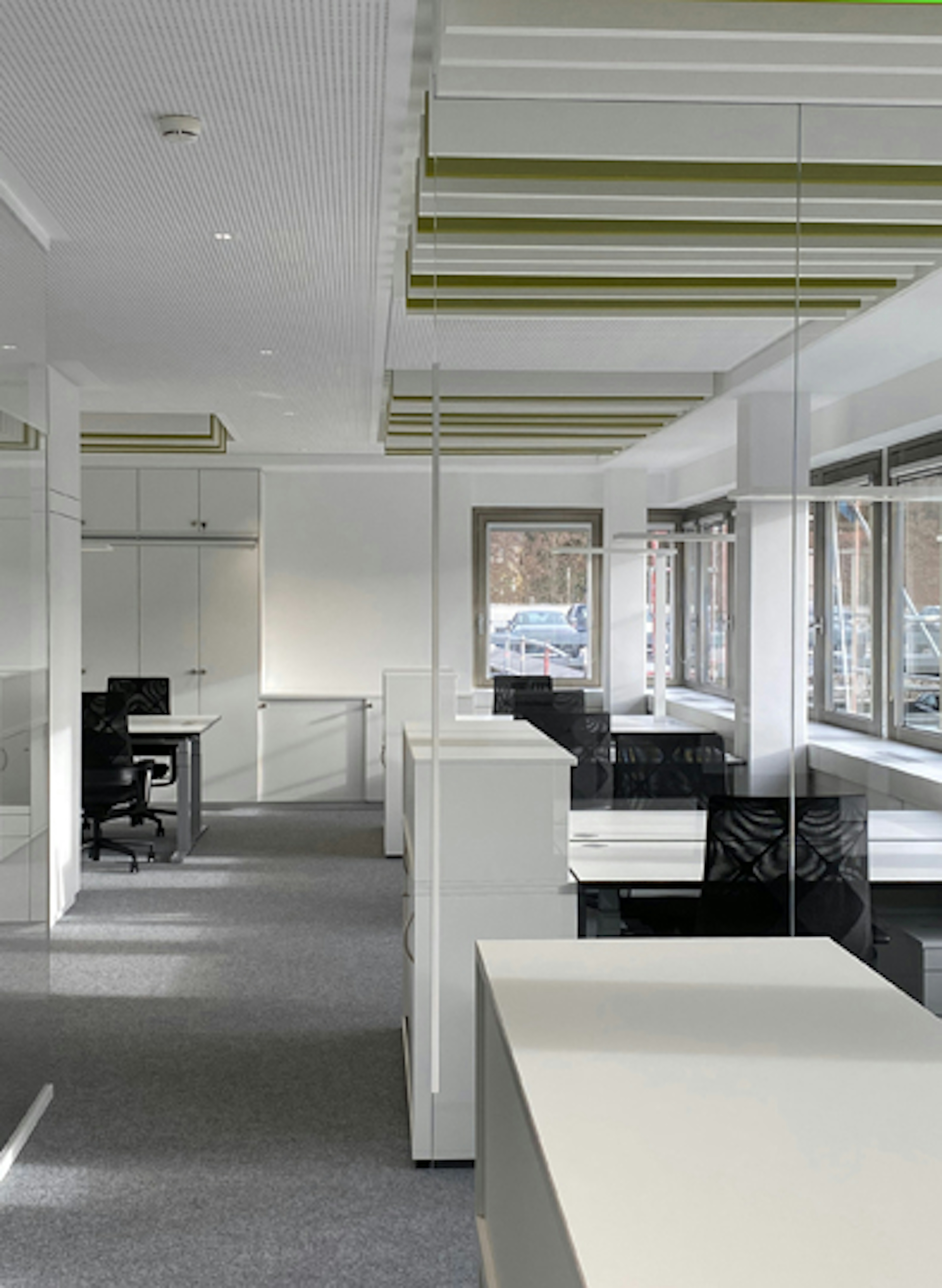 Reihe von ergonomischen Schreibtischarbeitsplätzen entlang großer Fensterfronten mit Blick auf den Außenbereich.