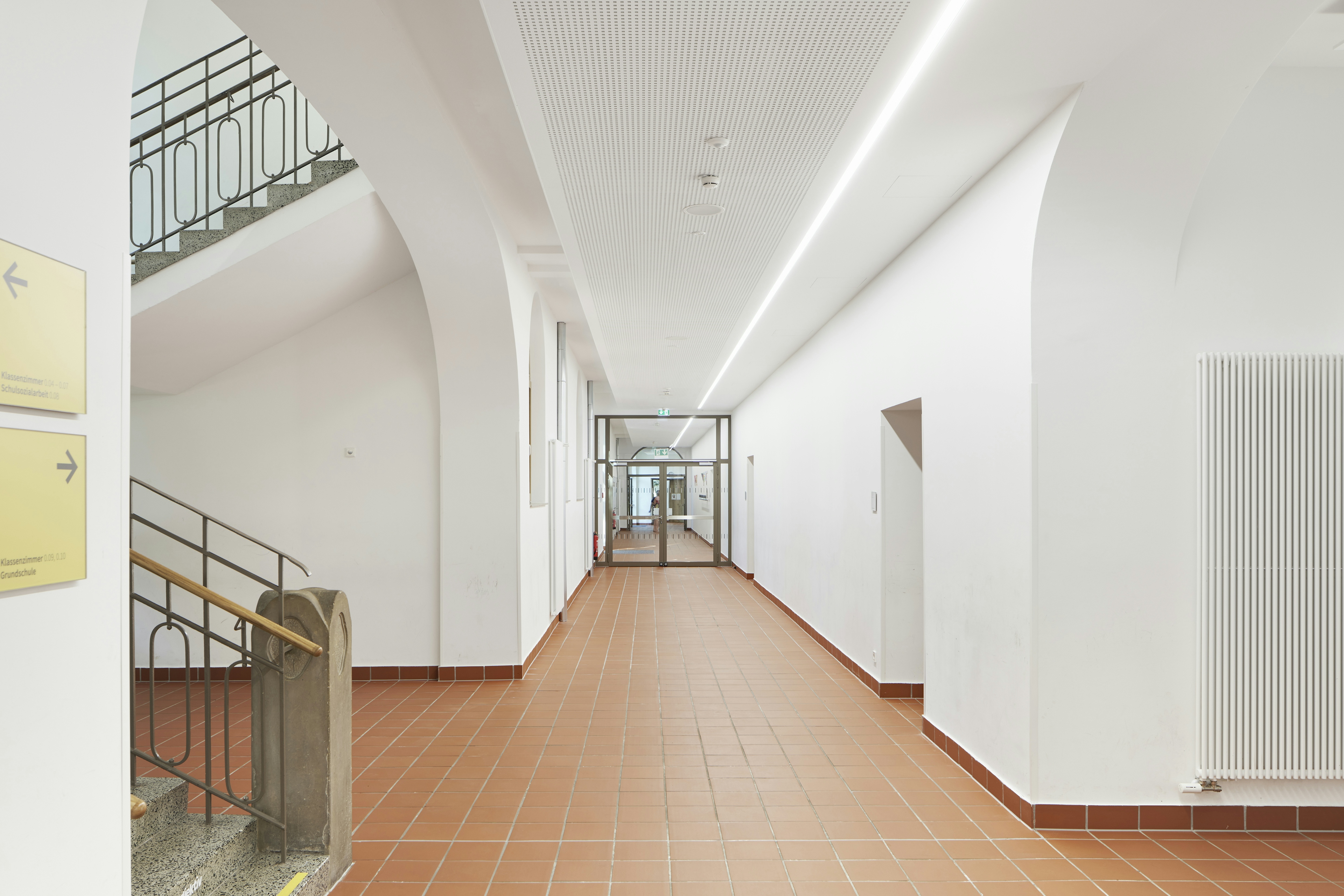 Sanierter Flur der Dammschule Heilbronn mit neuer LED-Beleuchtung, weißer Akustikdecke und rutschfestem Klinkerboden, Blick in Richtung Eingangstür mit Glaselementen.