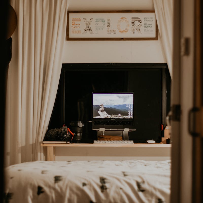 A makeshift desk on a small shelf next to a bed in an RV.