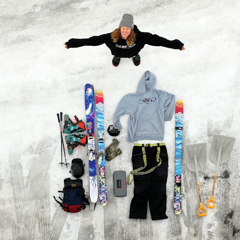 Ryan standing in an overhead shot of his ski gear laid out on the ground.