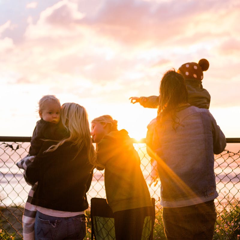 Amber Thrane and her family watching the sun set by a fence, with the beach & ocean in the background.