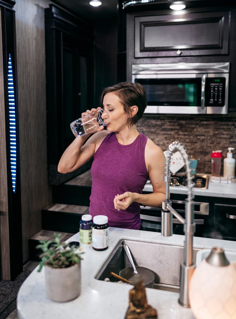 A woman in an RV kitchen taking vitamins with a glass of water.