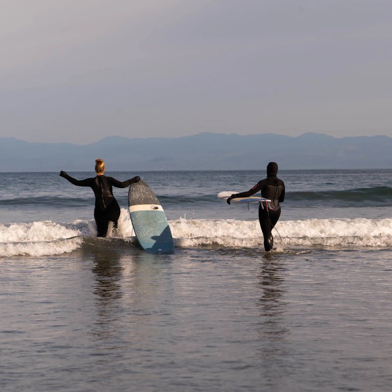 Chlesea and Layla walking into the ocean with surf boards