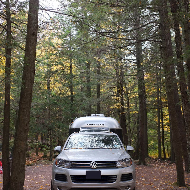 Dr. Na's Airstream and car parked in a wooded campsite.