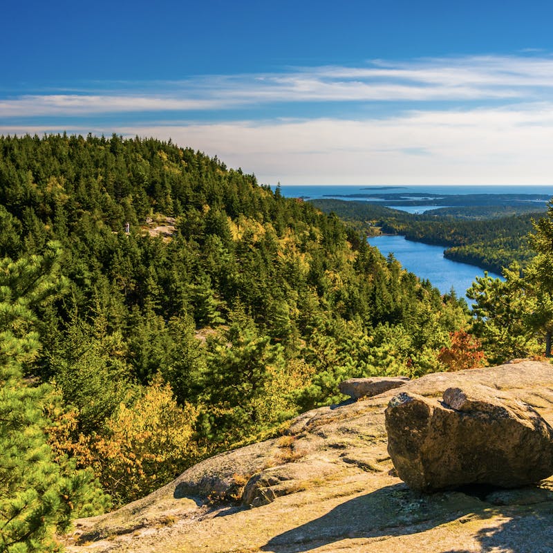 View from the top of a rock overlooking green pines, blue river and deep ocean in the distance