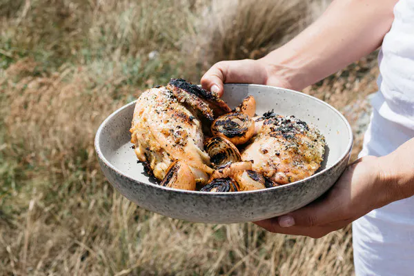 Close up of hands holding a bowl of cooked chicken and grilled vegetables.
