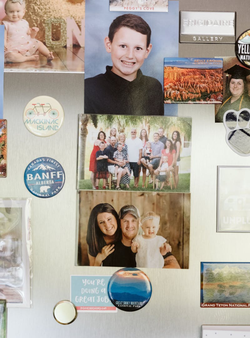 School pictures, family photos, baby pictures and stickers with destination names on them stuck on a stainless steel fridge.