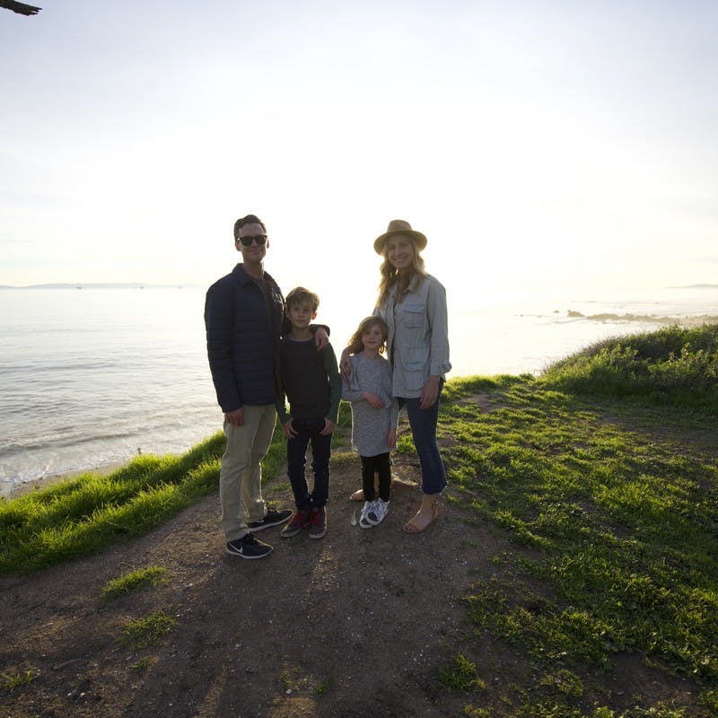 Family portrait of Sarah Schulz and her family on a clifftop, in front of the ocean during sunset.