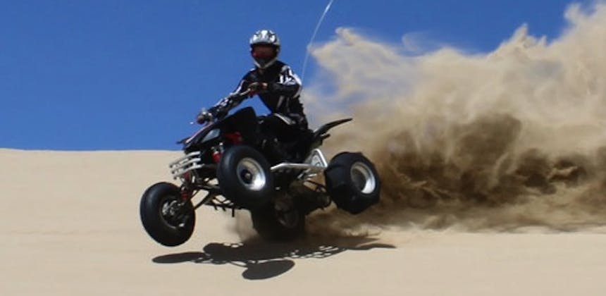 A quad bike rider throwing up sand at Oceano Dunes.