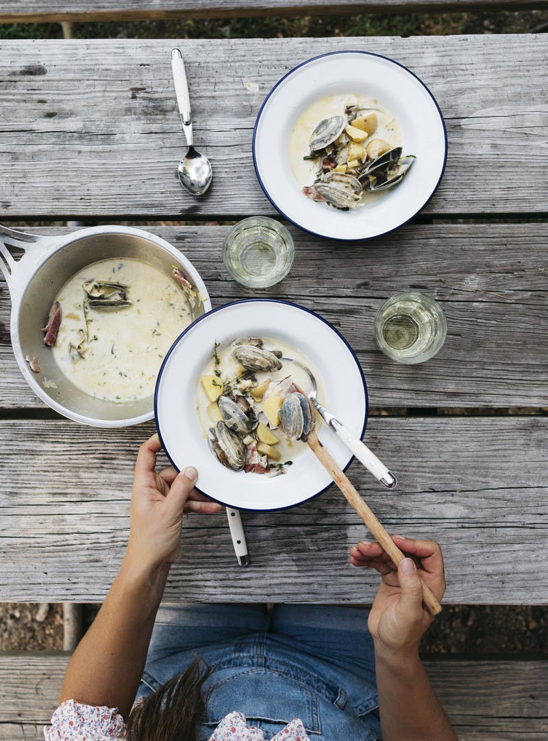 Sarah serving herself a bowl of chowder at a weathered outdoor picnic table.