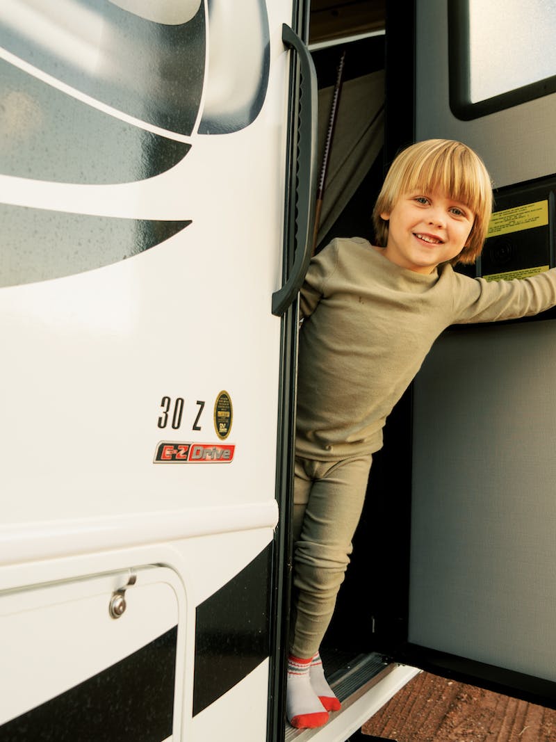 Little boy opens front door of Thor Class C motorhome and smiles out at the camera