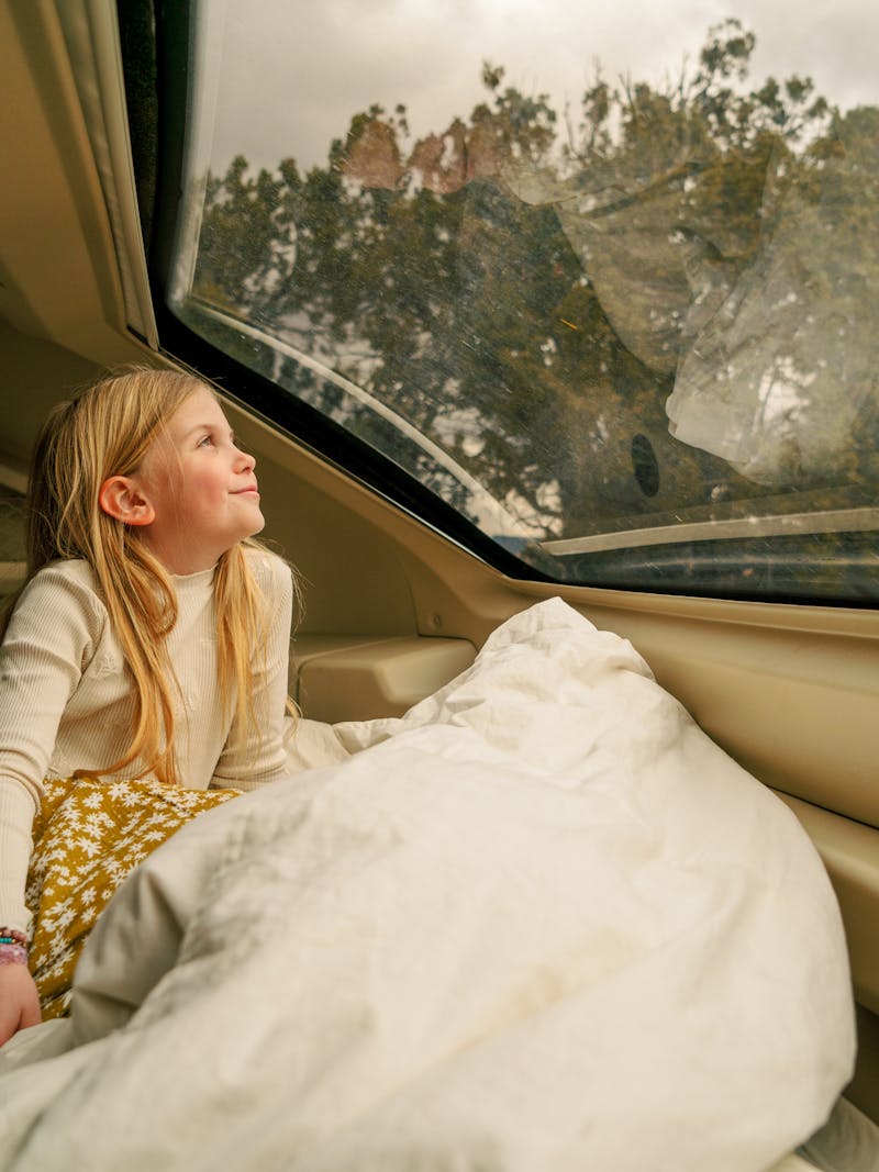 A young girl looks out the window of an RV at the view.