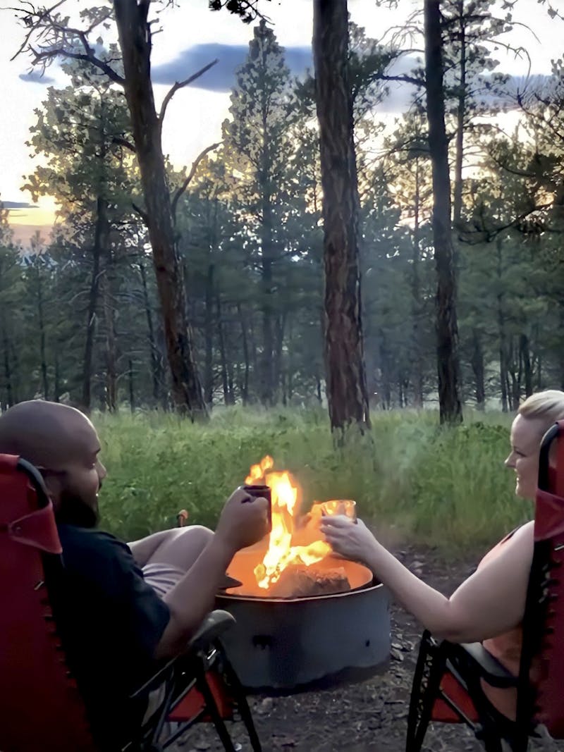CHRISTINA AND BEN MCMILLAN sit around a campfire while cheersting