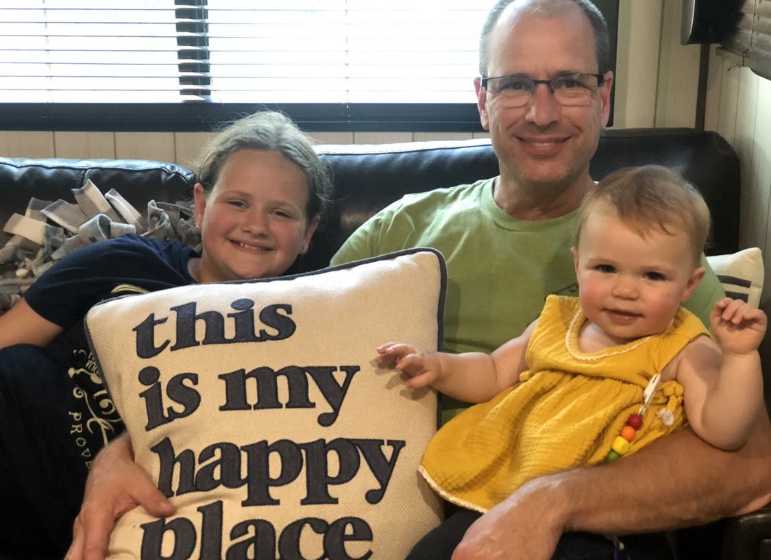 A middle aged man sitting with his two grandkids on a couch.
