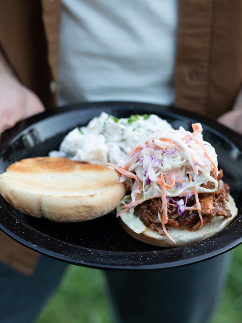 A close up of a barbeque pulled pork sandwich with coleslaw and potato salad.