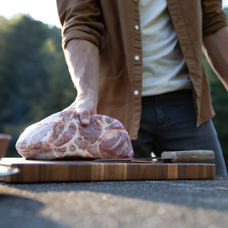 A man places a big slab of pork on a cutting board.