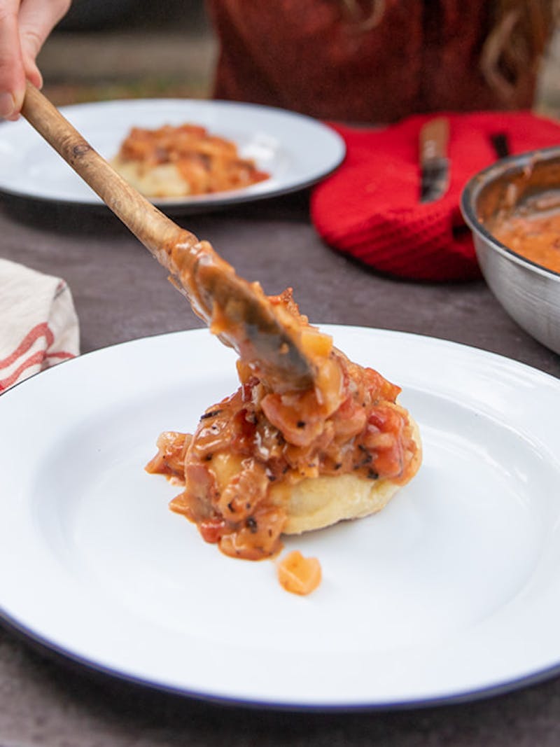 Spooning tomato gravy over a fresh biscuit on a plate.