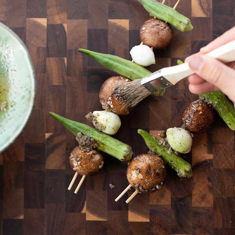 Brushing mushrooms and okra kabobs with oil and seasonings.