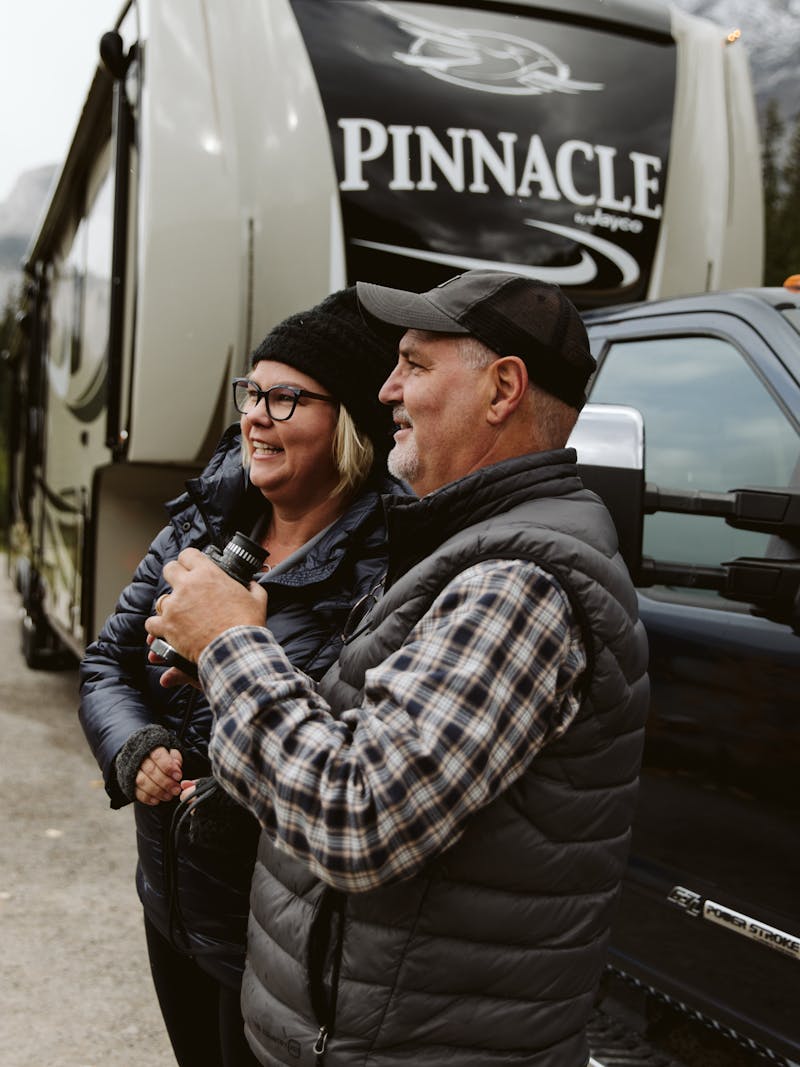 Tina and Craig Klinefelter standing outside their RV with binoculars, looking for wildlife.