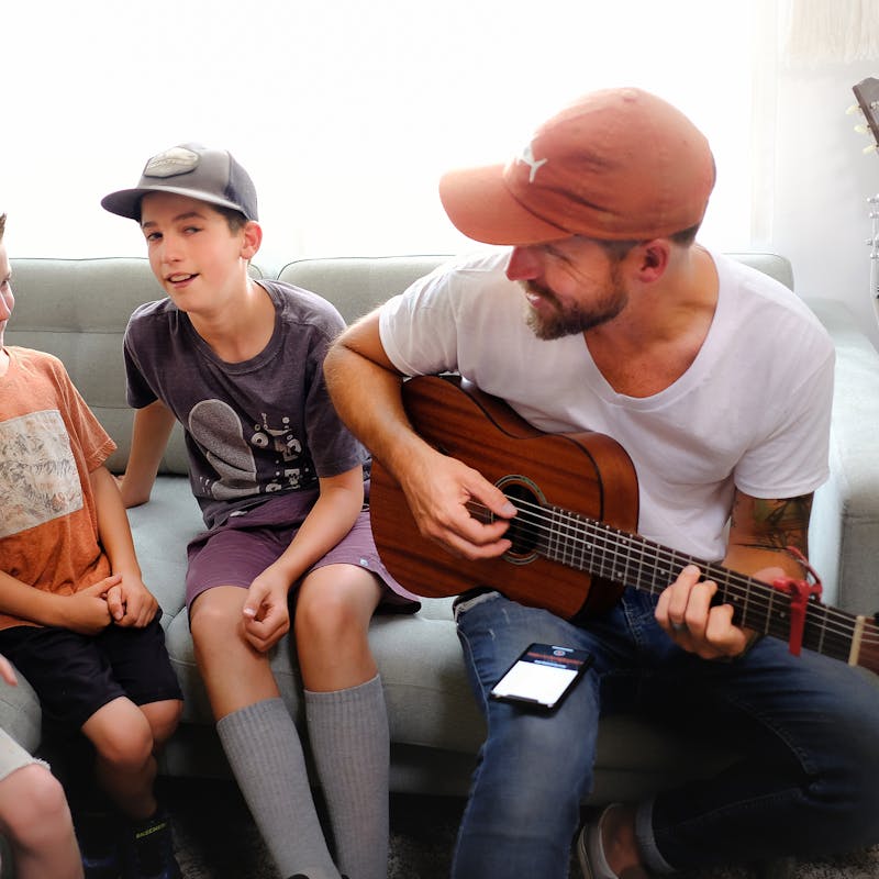 Amick Cutler plays guitar while his three sons sing along while sitting on a couch in their RV.