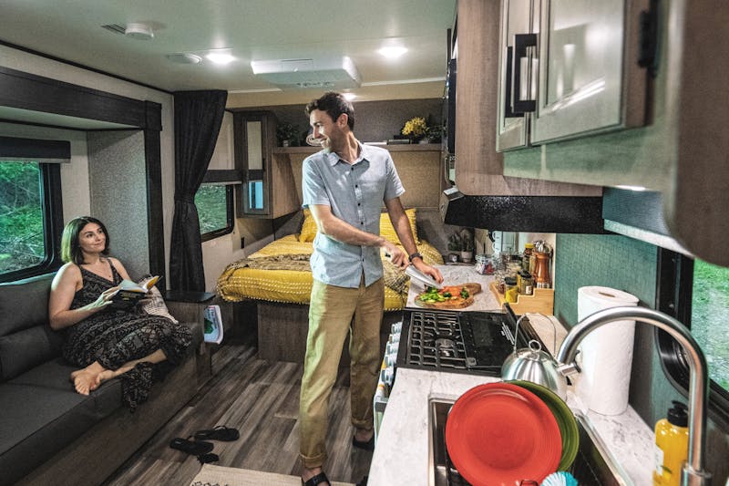 A woman lounges on a couch inside a Starcraft RV while a man chops vegetables at a counter 