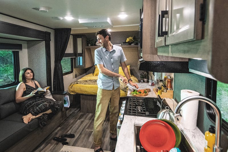 A woman lounges on a couch inside a Starcraft RV while a man chops vegetables at a counter