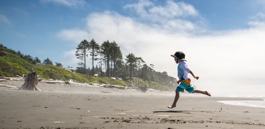 Young boy jumping and skipping on ocean beach with trees in the background