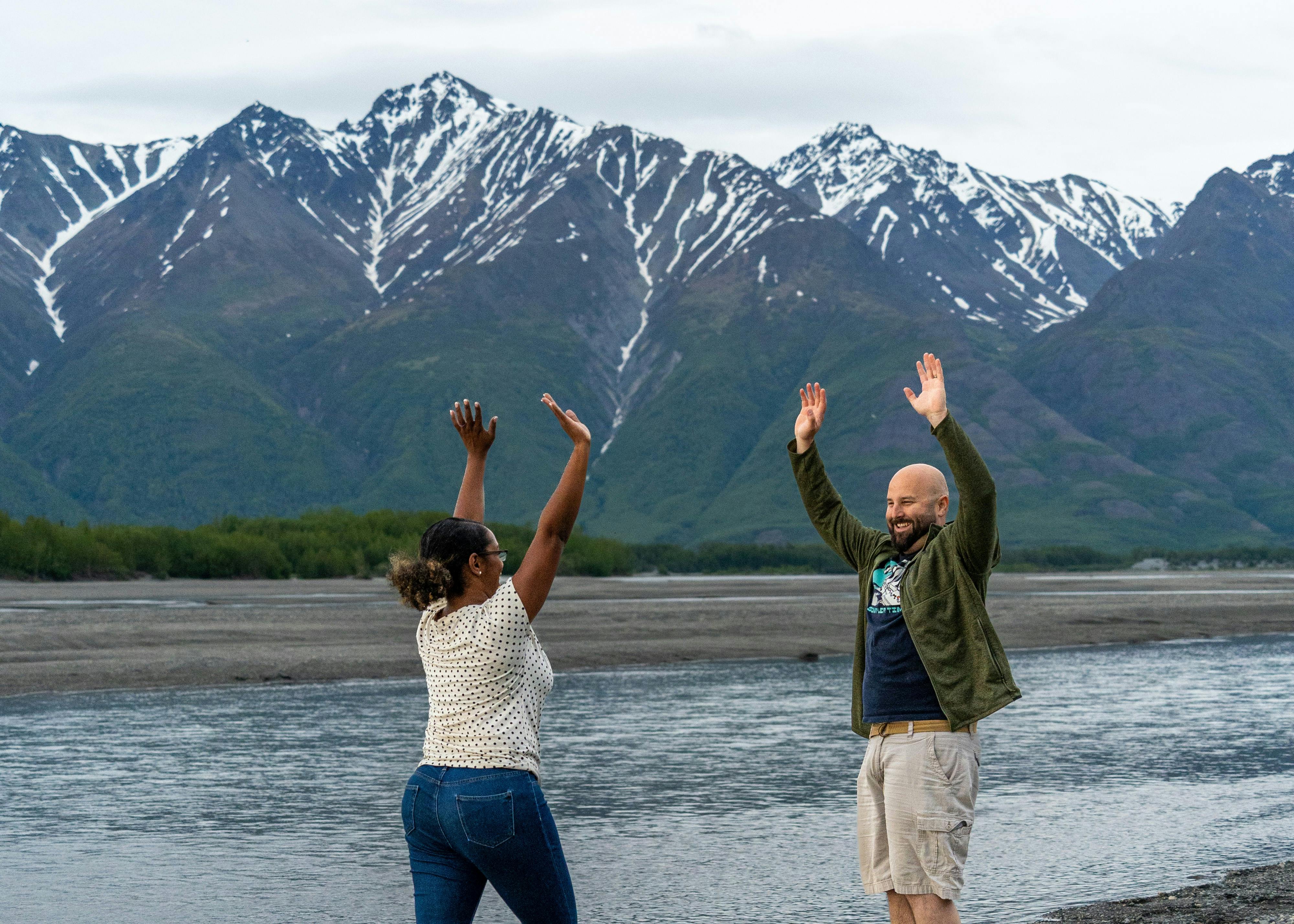 Gabe and Rocio Rivero smiling with their arms raised in front of mountains