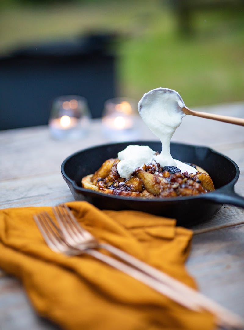 Spoon putting whipped cream on top of the finished bananas foster dish.