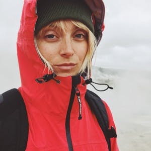 Laura Austin, wearing a red rain jacket with a hood up, takes a selfie with a serious face.