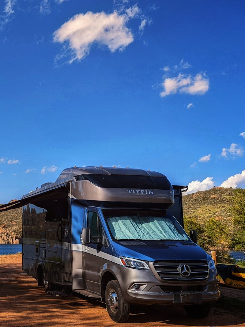 Dustin and Sarah Bauer's Tiffin Wayfarer parked at a campsite under blue skies by a lake