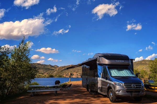 Dustin and Sarah Bauer's Tiffin Wayfarer parked at a campsite under blue skies by a lake 