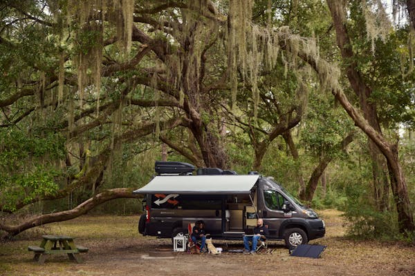 Gabe and Rocio sitting outside of their RV under a large oak tree